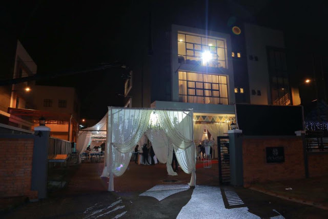 Nighttime exterior of a multi-story building with a white draped tent entrance and lights, dark moody atmosphere