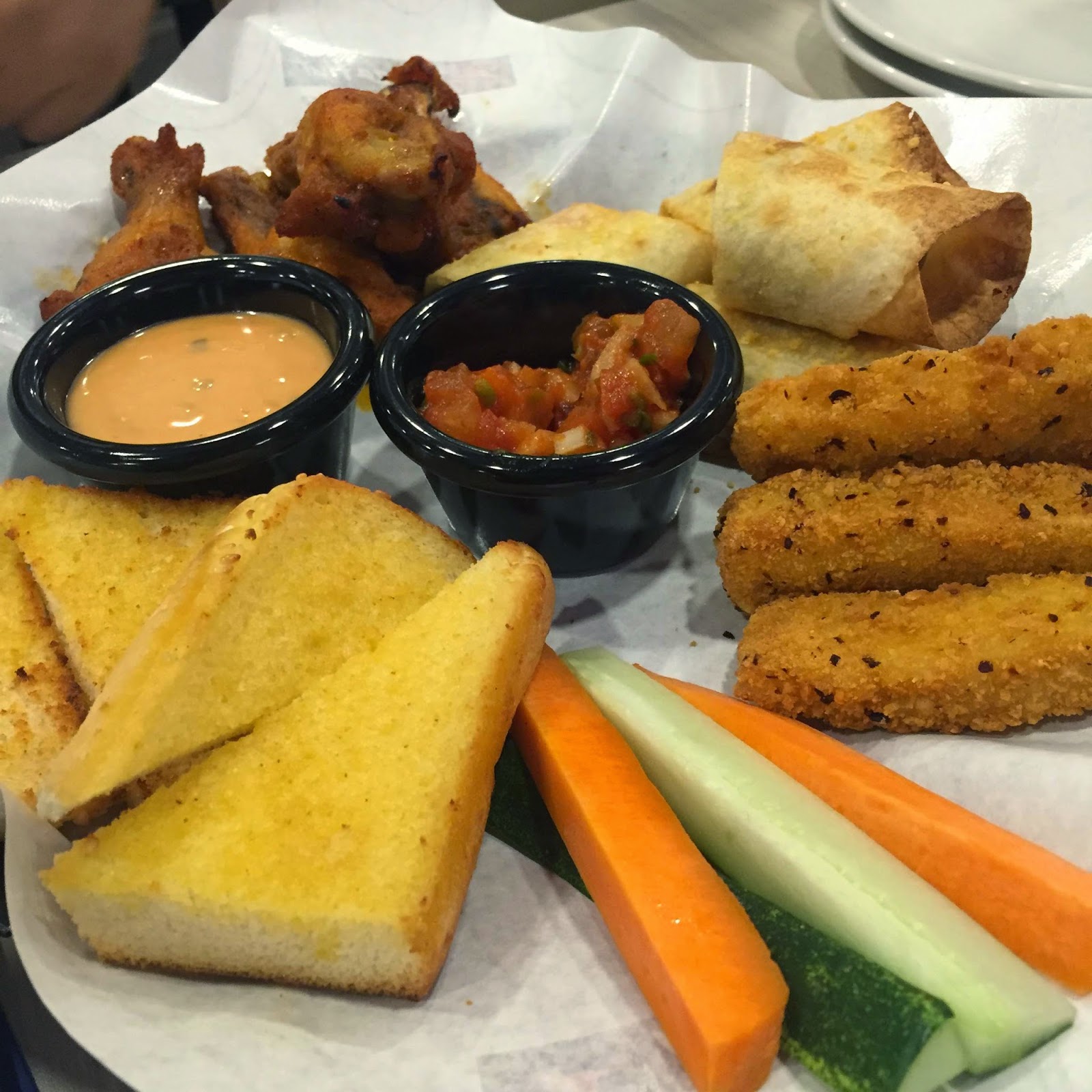 Platter of fried appetizers including chicken wings, egg rolls, breaded sticks, cornbread and dipping sauces with vegetables, warm inviting mood