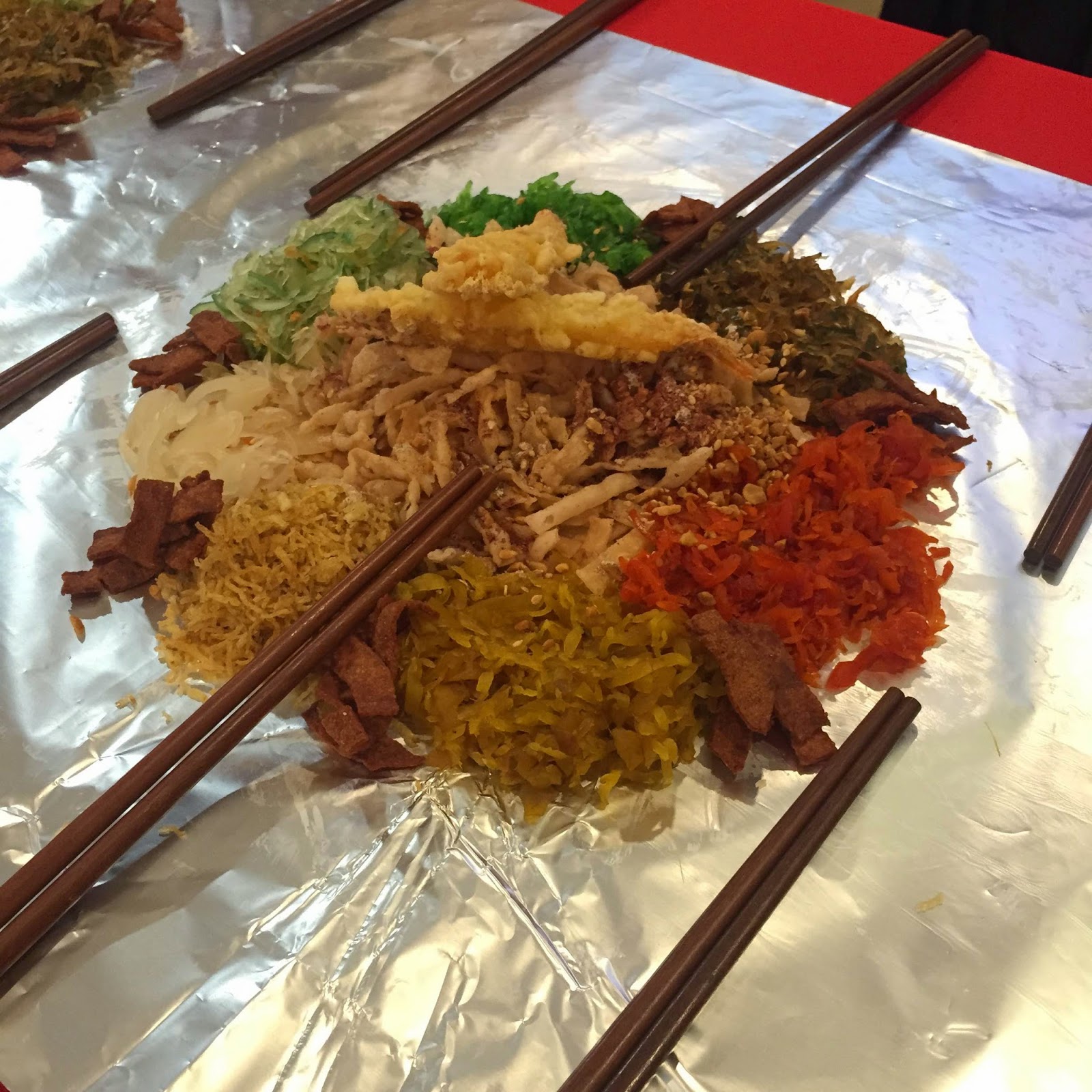 Overhead shot of a colorful shredded salad dish with many ingredients spread on foil, surrounded by chopsticks, festive mood